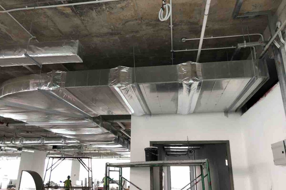 Exposed industrial ceiling with ductwork and pipes, partially wrapped in plastic, in an unfinished building space.