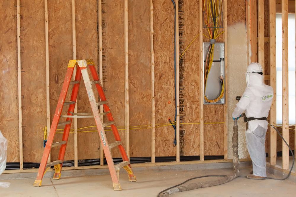A man in a white suit is renovating a room with wooden walls, focused on his work.