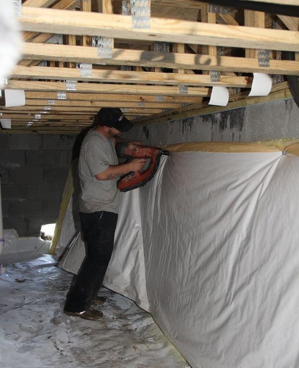 A man is repairing a wall in a dimly lit basement, focused on his work with tools in hand.