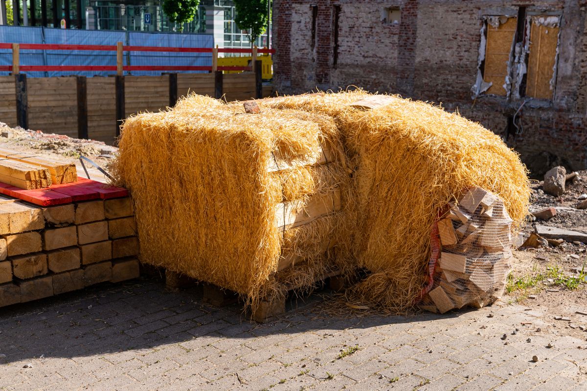 A large pile of hay, used for insulation services, is stacked neatly in a sunny outdoor setting.